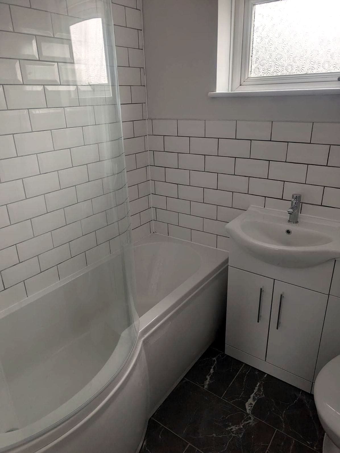 Finished bathroom: white metro tiles, a shower screen over the bath and a vanity basin