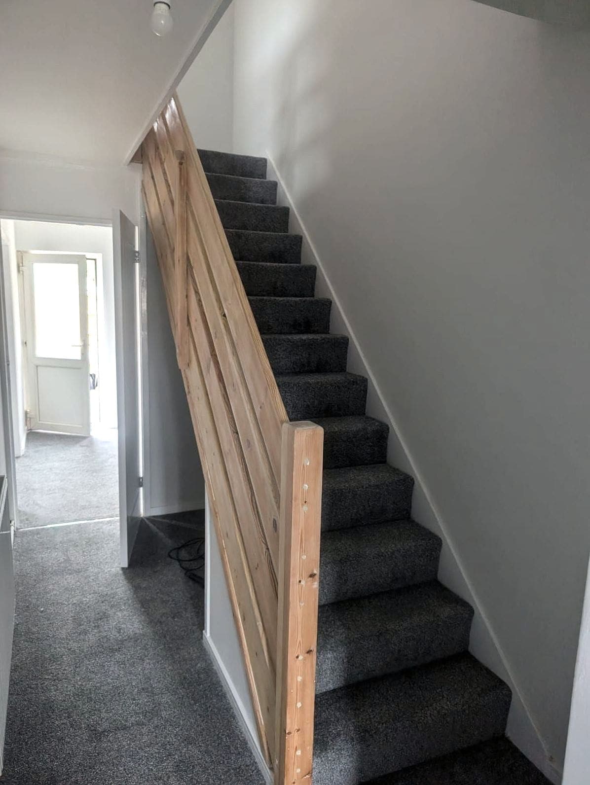 Hall and stairs finished: grey stair carpet and a timber handrail