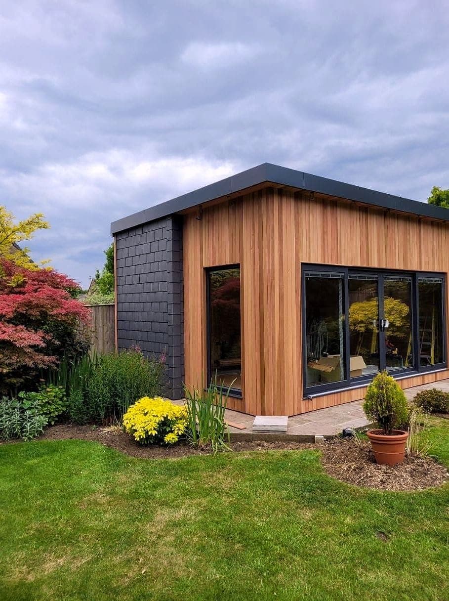 Cedar-clad garden room with dark sliding doors, standing on a lawn