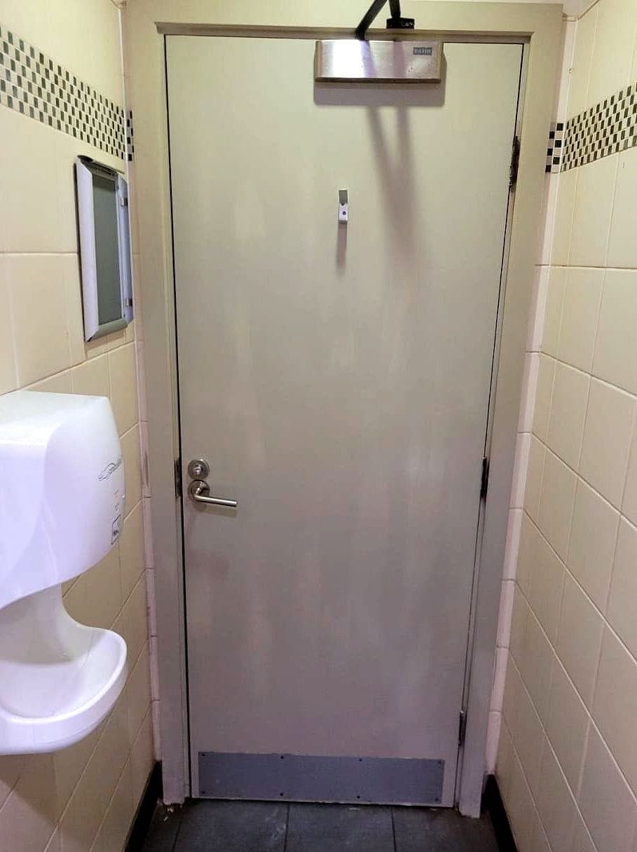 The washroom door hung and closed, with a closer and kick plate