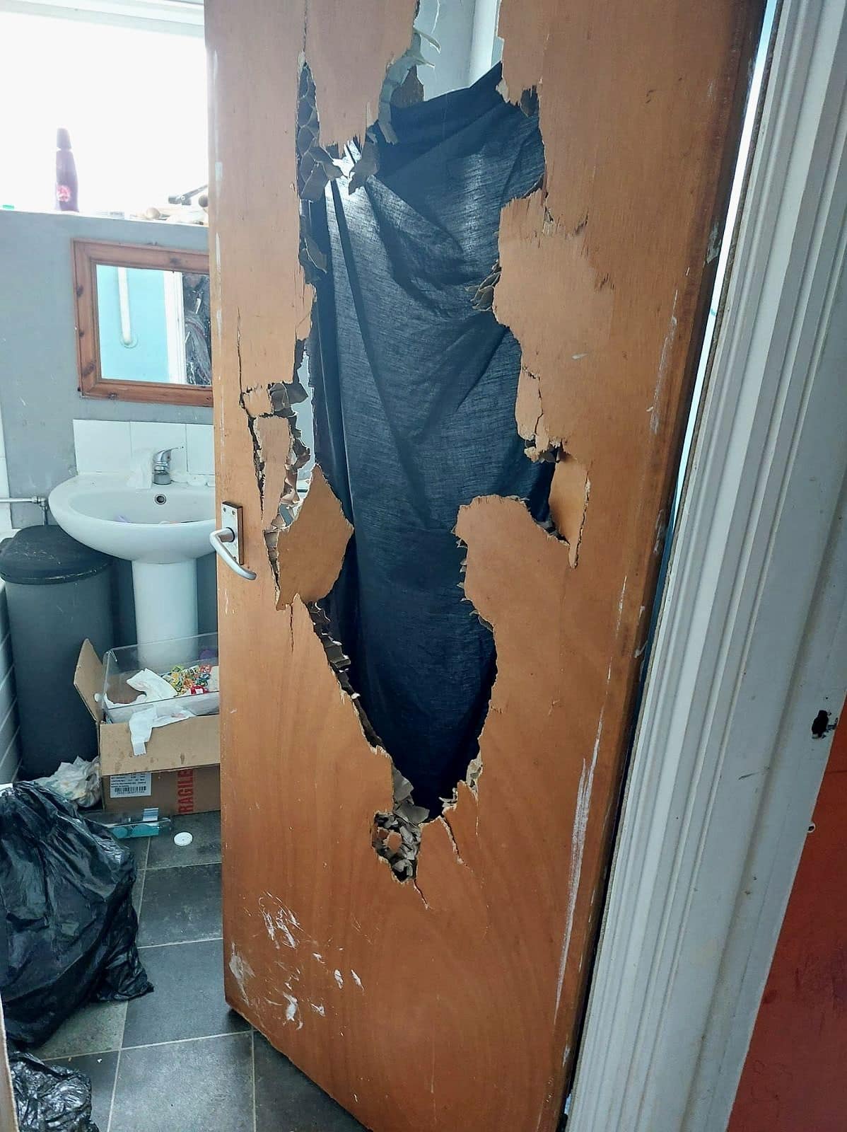 Bathroom door punched through, with bin bags in the bathroom behind