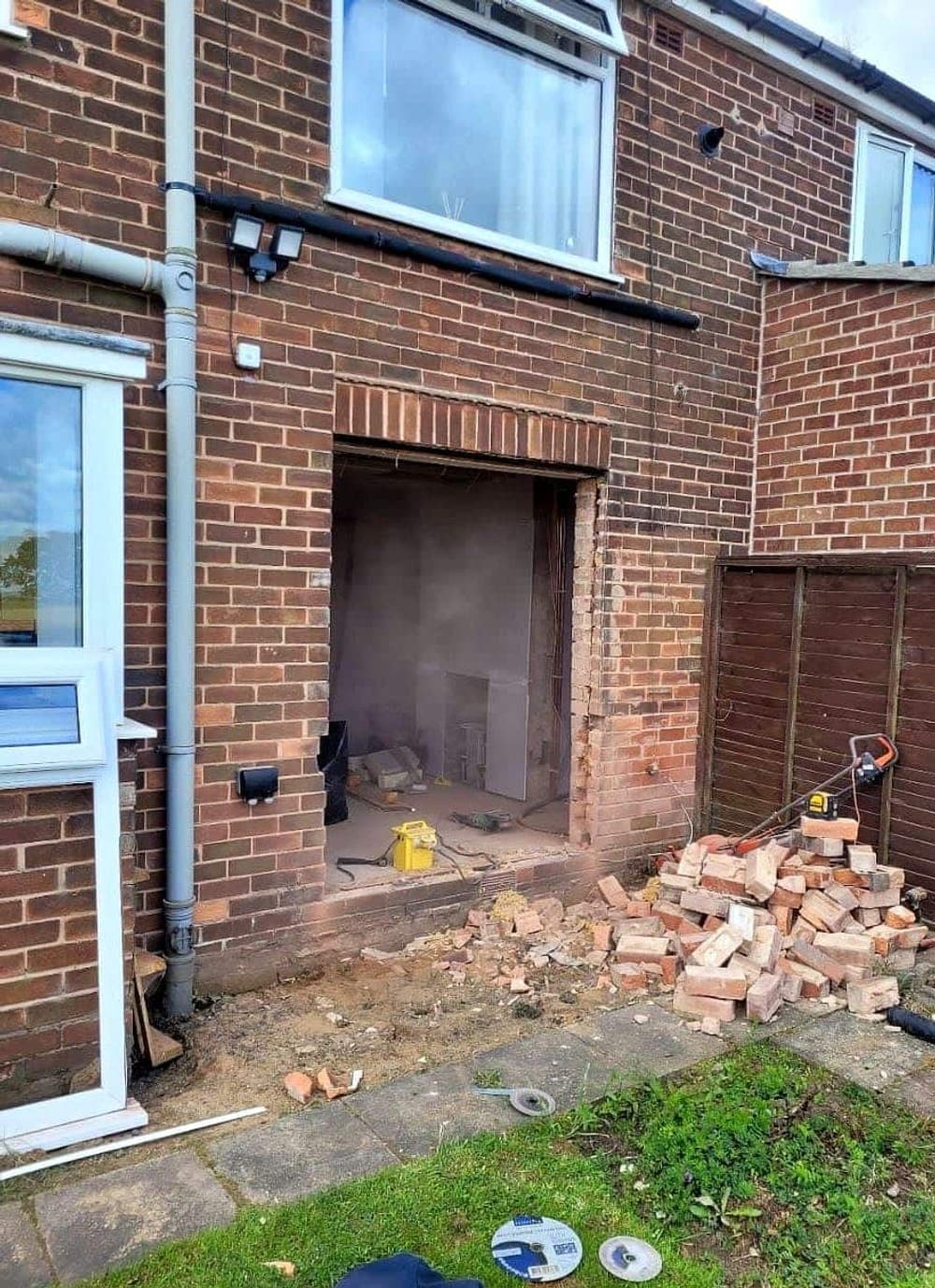 Rear brick wall with the new opening cut, bricks stacked on the grass